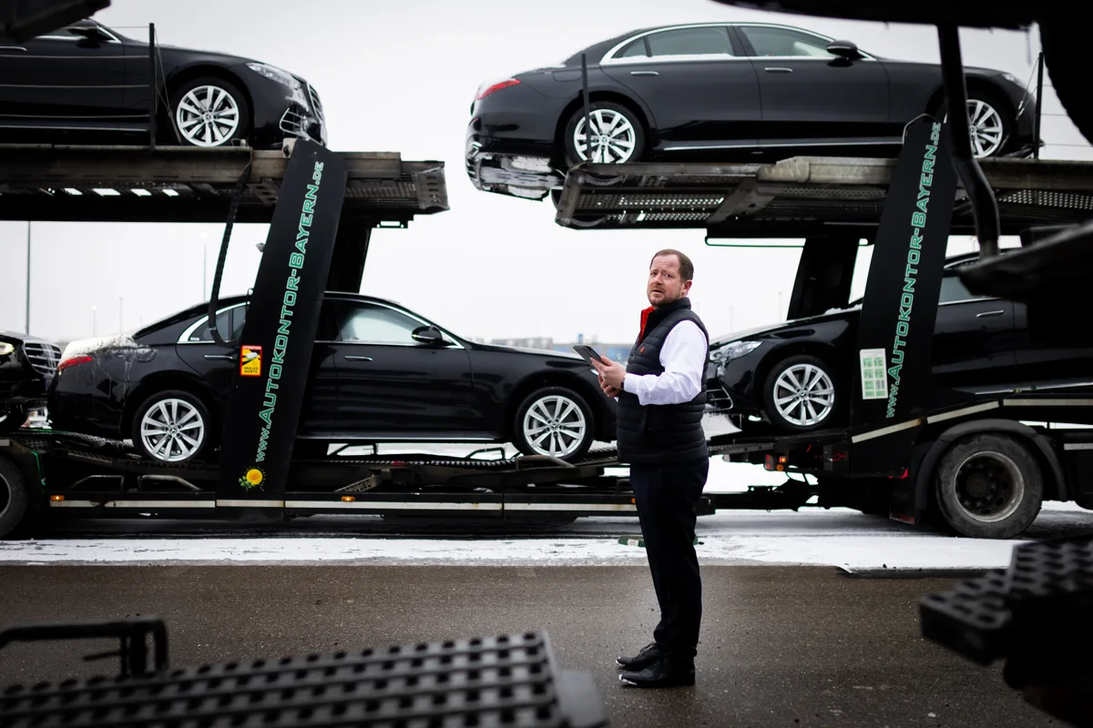 Ein Mann steht neben einem Autotransporter mit schwarzen Edellimousinen.